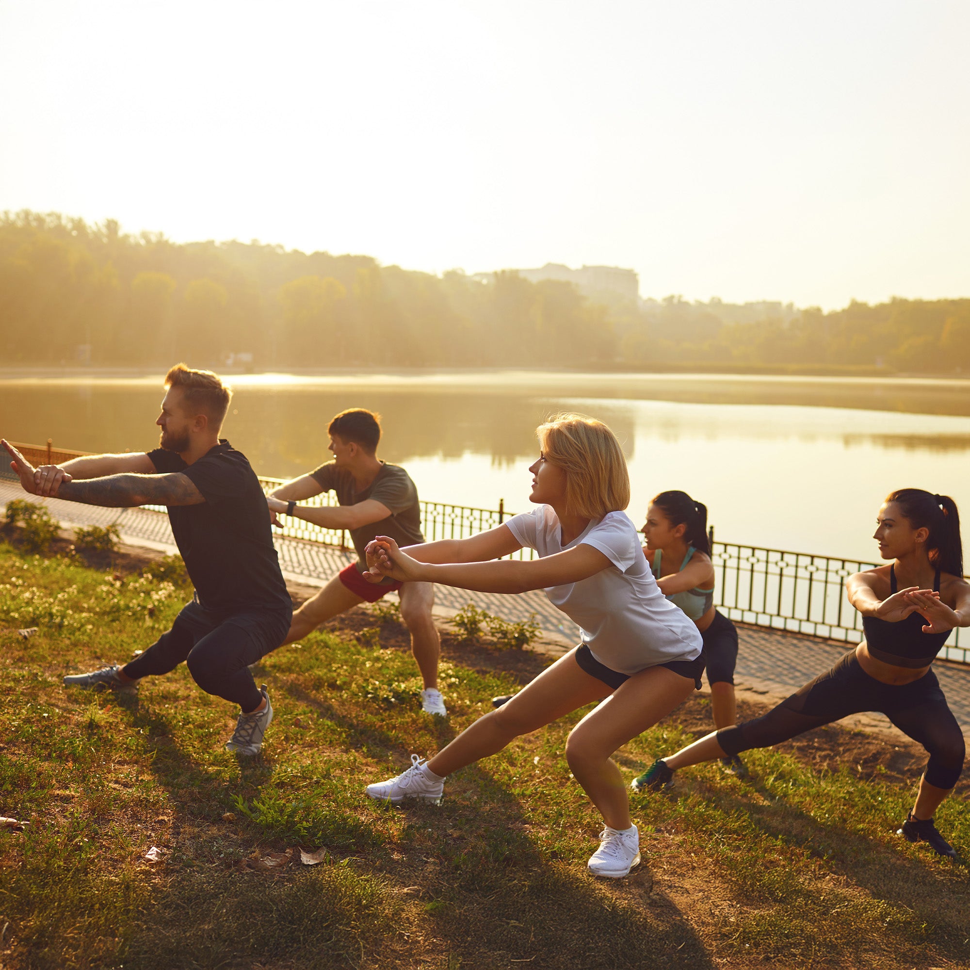 Vier Personen machen Sport auf einer Wiese an einem See in der Sonne