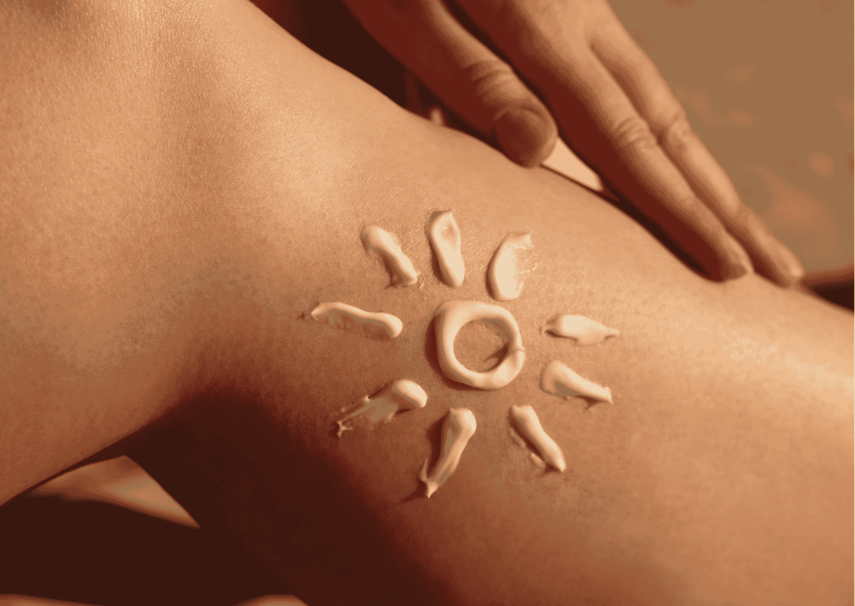 Sonnencreme in Form einer Sonne auf der Haut, Nahaufnahme; Hand streicht über den Oberschenkel, Fokus auf Hautpflege