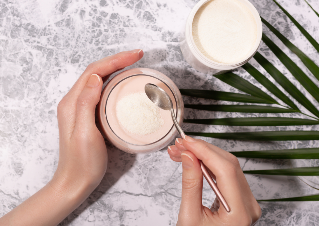 Zwei weibliche Hände füllen weißes Kollagenpulver in ein Getränk