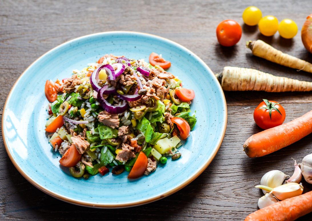 Bunter Gemüsesalat mit Tomaten, Gurken, Zwiebeln und Kräutern auf blauem Teller; frische Zutaten auf Holztisch