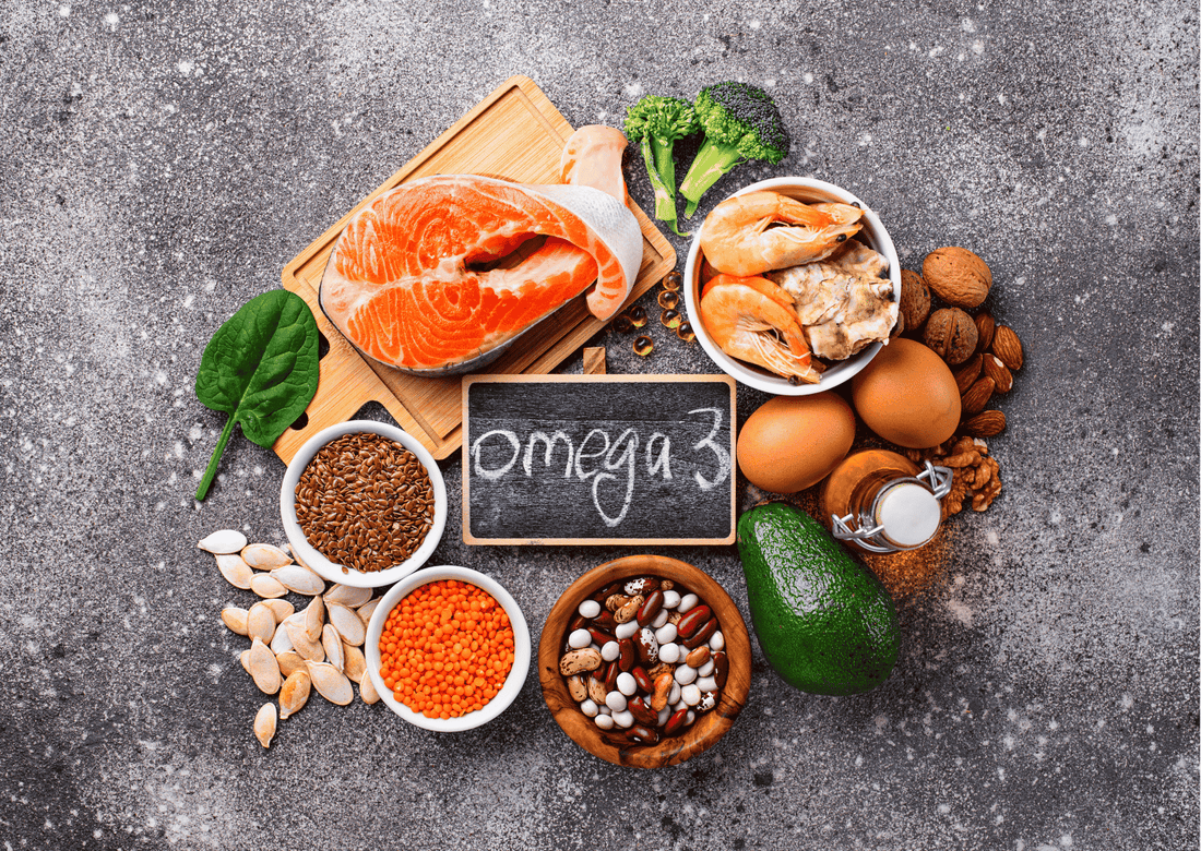 Auswahl omega-3-reicher Lebensmittel wie Lachs, Nüsse, Avocado und Samen; Tafel mit Aufschrift „Omega 3“