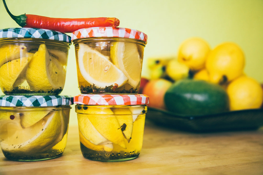 Gläser mit eingelegtem Gemüse und Zitrusfrüchten auf Holztisch; fermentierte Lebensmittel und gesunde Küche