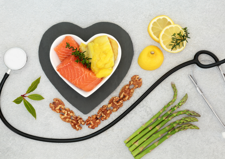 Herzförmig angerichtete Lebensmittel wie Lachs, Avocado und Zitrone mit Stethoskop; Symbol für herzgesunde Ernährung