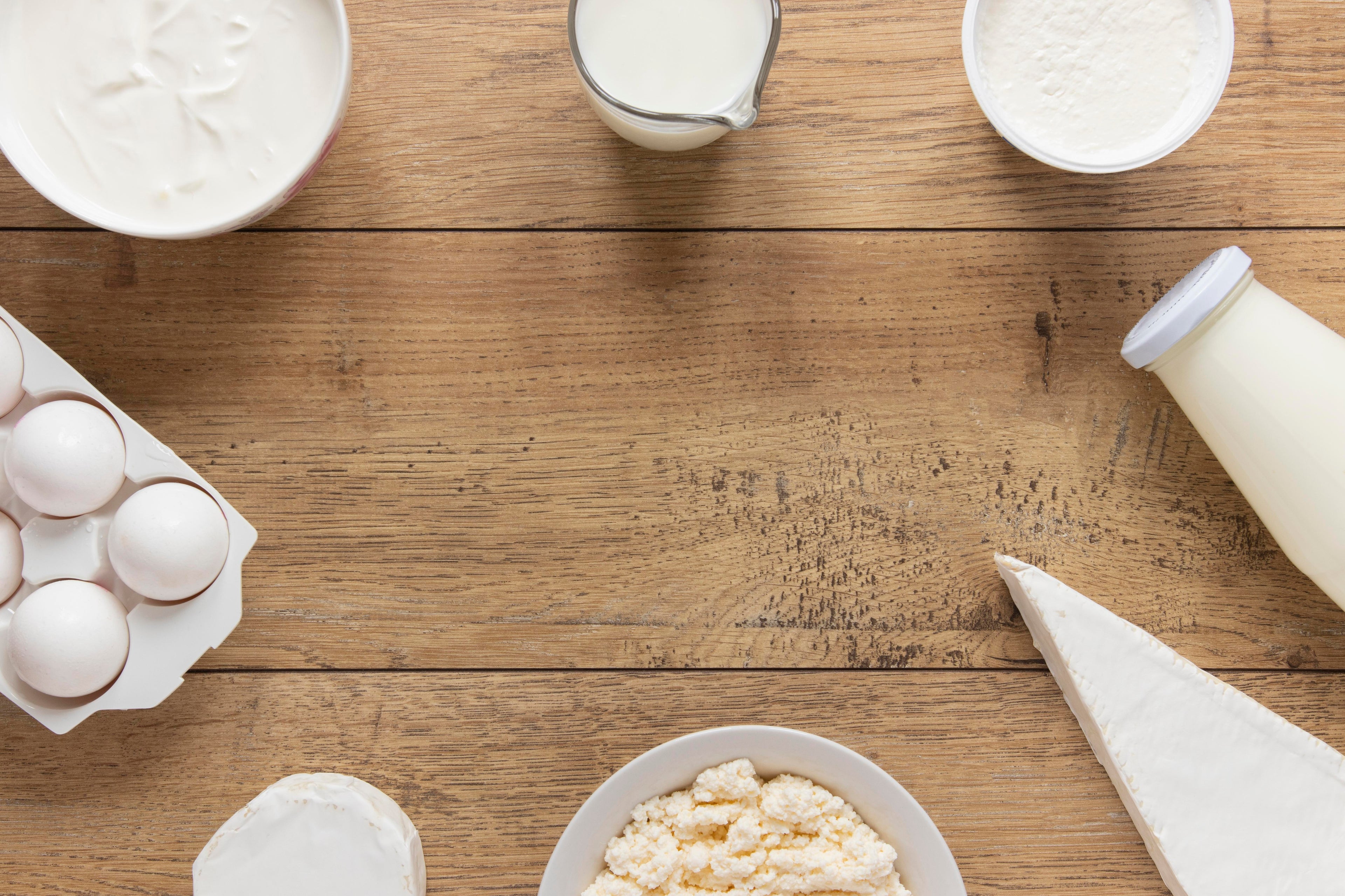 Milchprodukte wie Joghurt, Quark, Milch und Eier auf Holztisch angeordnet; Auswahl an Lebensmitteln mit Laktose