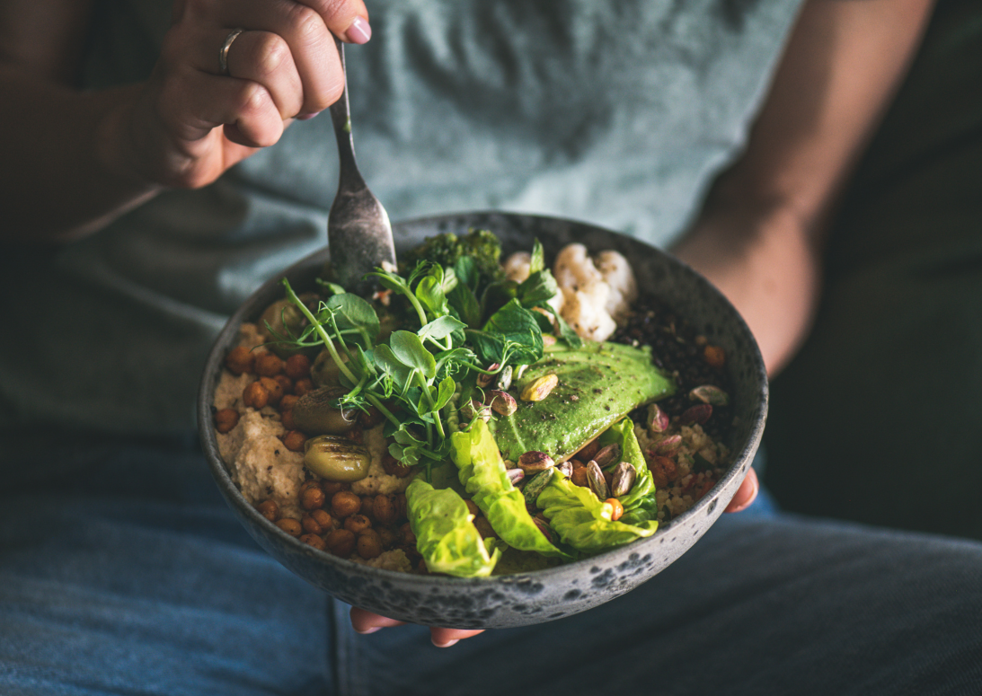 Person hält Schale mit gesunder Bowl aus Reis, Gemüse und grünem Spargel; ausgewogene pflanzliche Mahlzeit