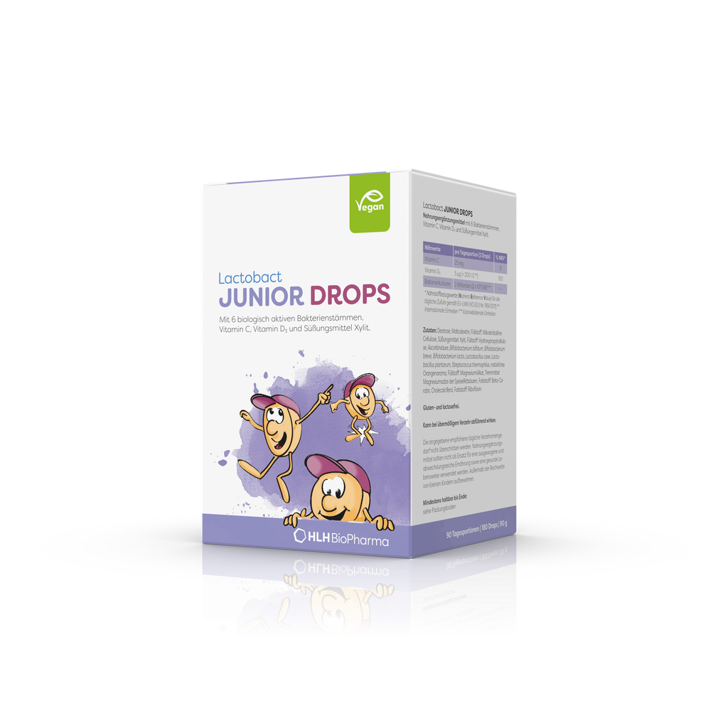 Produktbild schräge Ansicht von Lactobact JUNIOR DROPS 180 Drops mit lilafarbenem Aquarell Wasserfleck und 3 Karikaturen mit freundlichen Gesichtern und rosa Cappys auf der Verpackung.