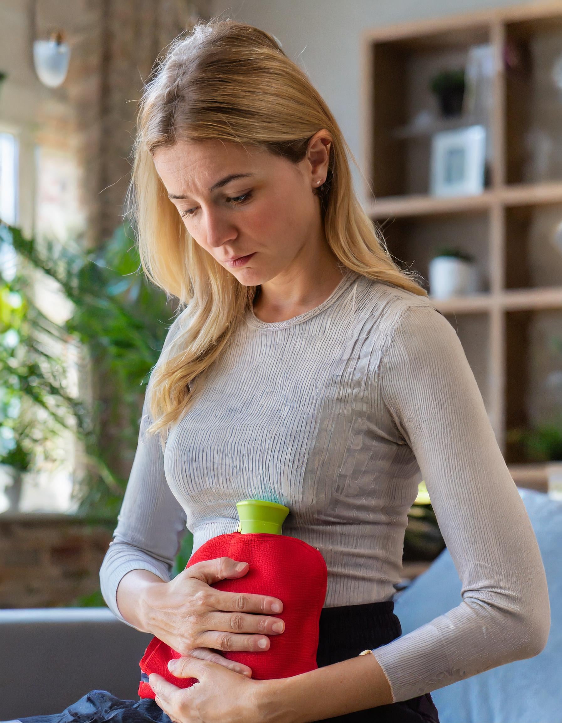 Blonde Frau sitzend mit Wärmflasche am Bauch