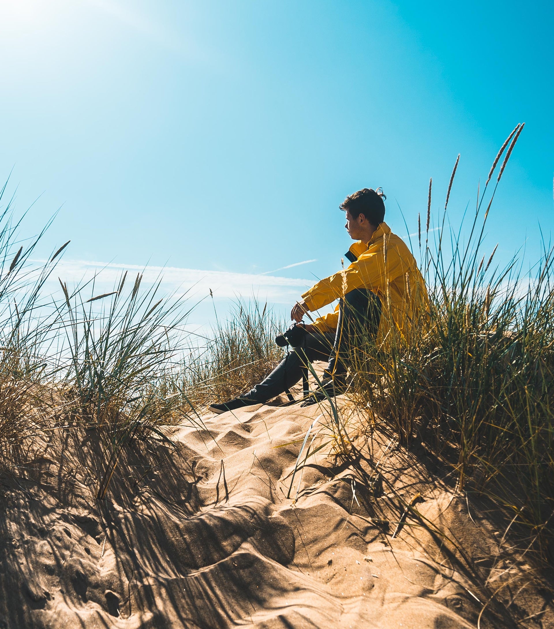 Mann mit gelber Jacke sitzt bei Sonnenschein in einer Düne