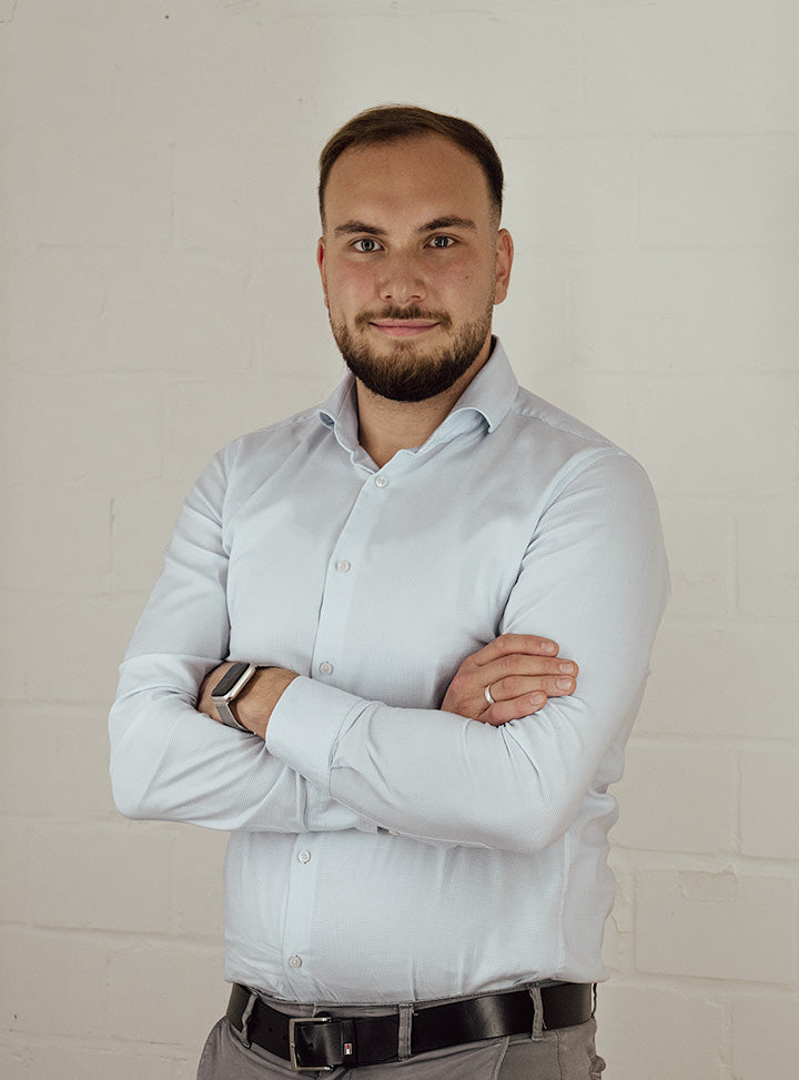 Serkan Cetin in hellem Hemd mit verschränkten Armen vor weißer Wand